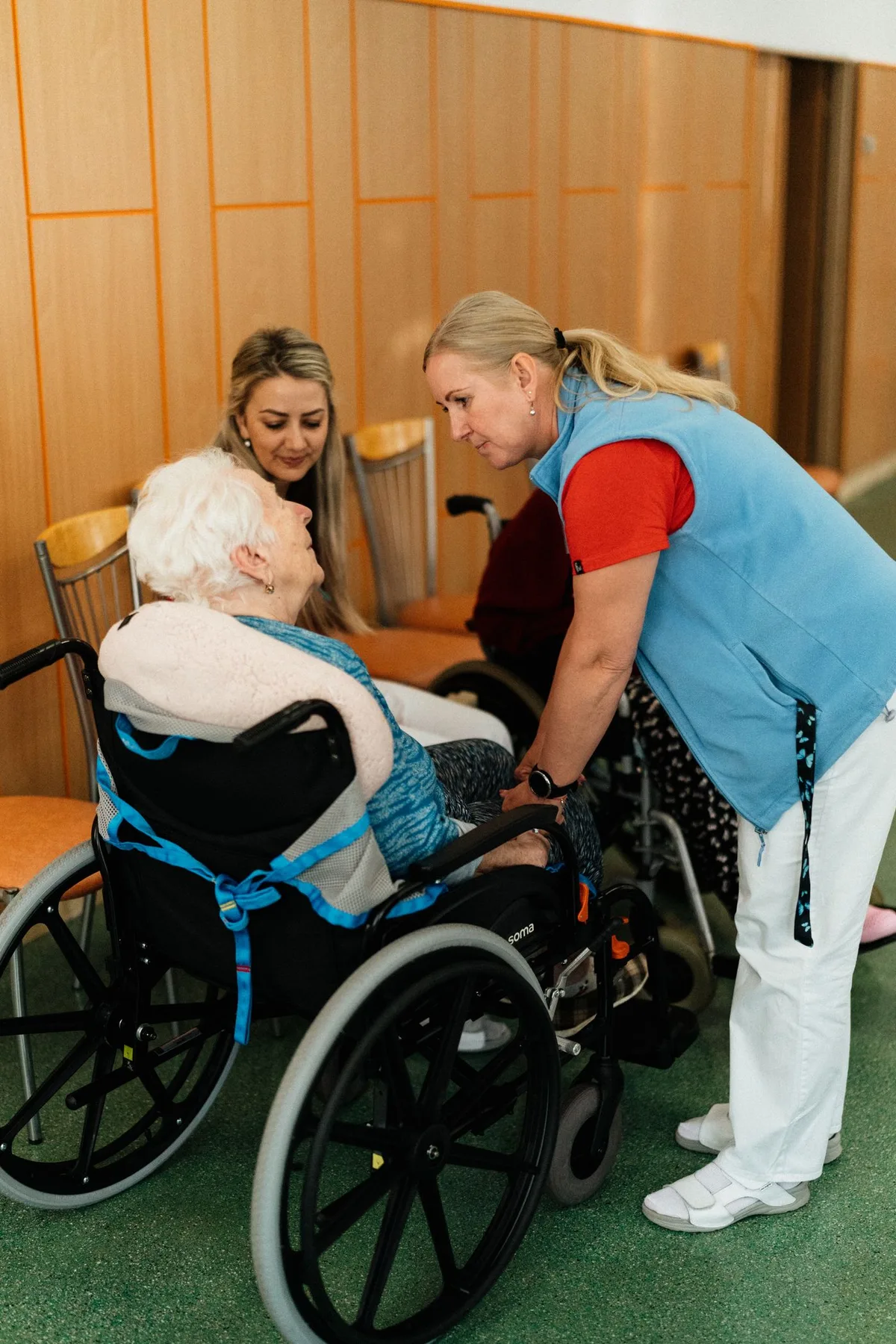 Eine Pflegekraft spricht auf Augenhöhe mit einer älteren Frau im Rollstuhl